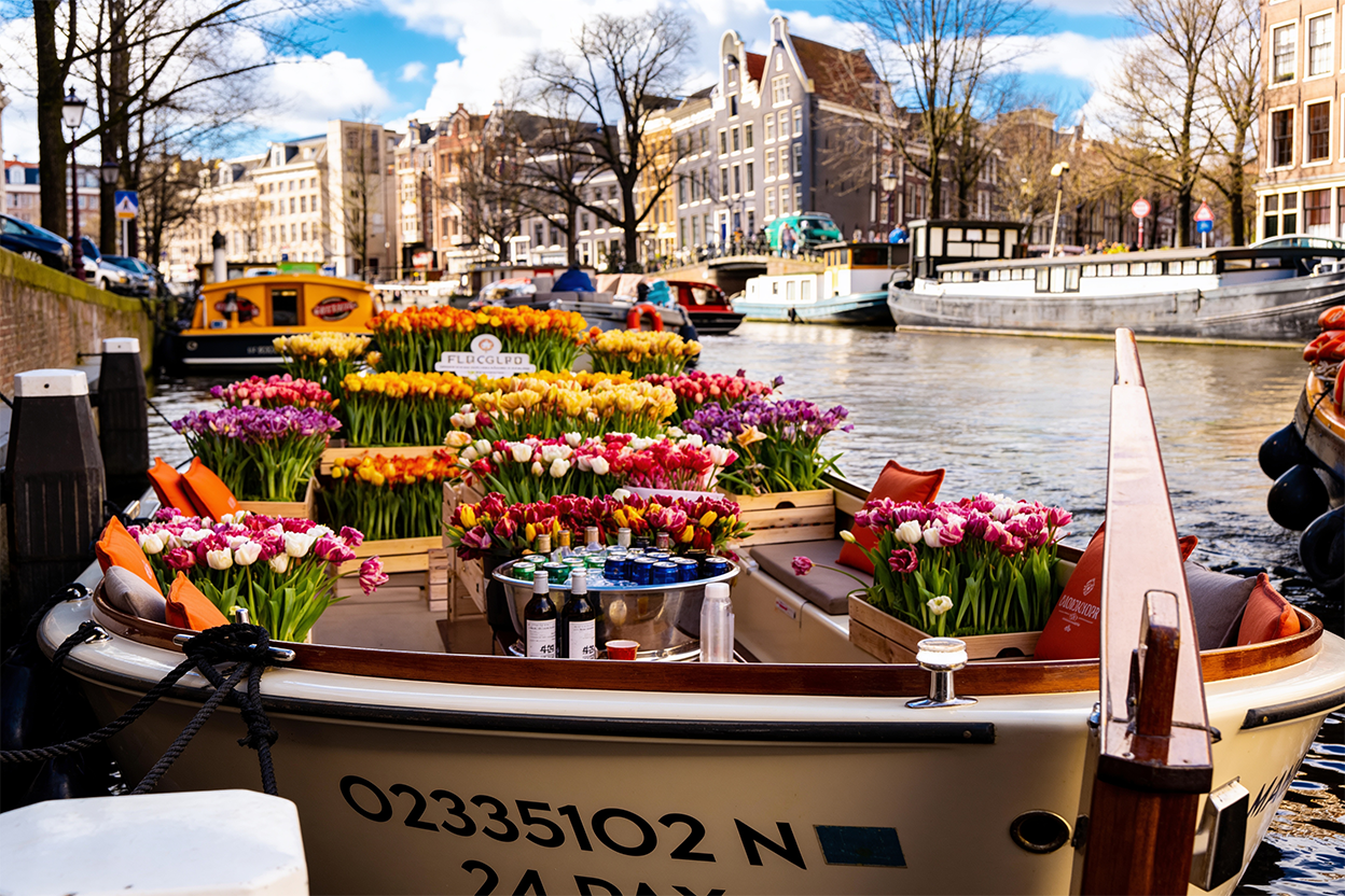 Persoonlijke tourplanning in Amsterdam waarbij een lokale gids samen met gasten aan een café aan de gracht verschillende touropties bespreekt, waaronder wandel-, fiets- en boottours.